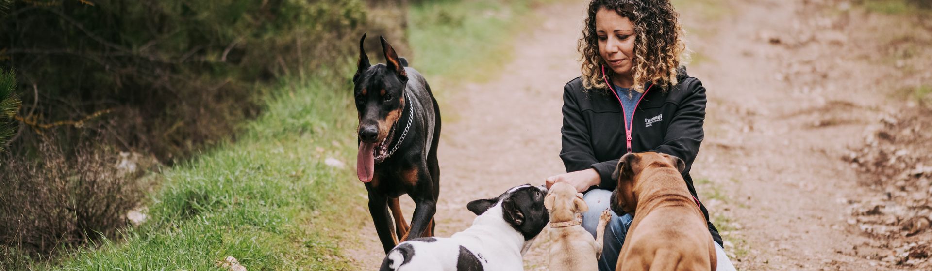 Donna accovacciata con tre cani su un sentiero di campagna
